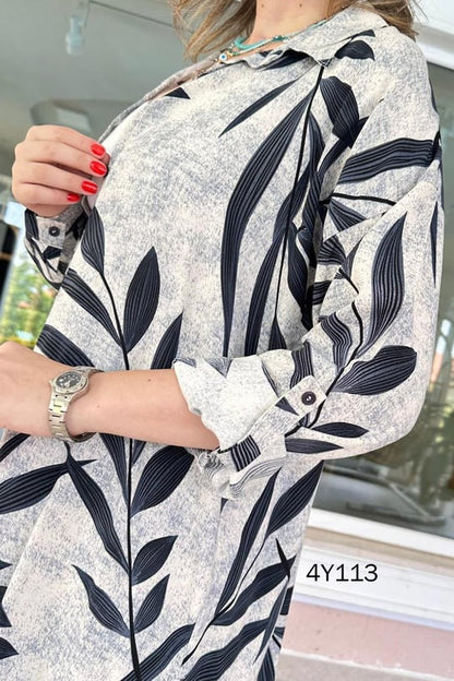 Close-up of leaf-print buttoned top, navy leaves on light fabric with rolled sleeve