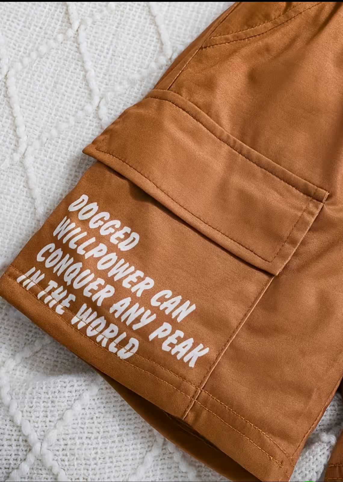 Brown cargo shorts with stitched seams, flap pockets, and printed slogan patch